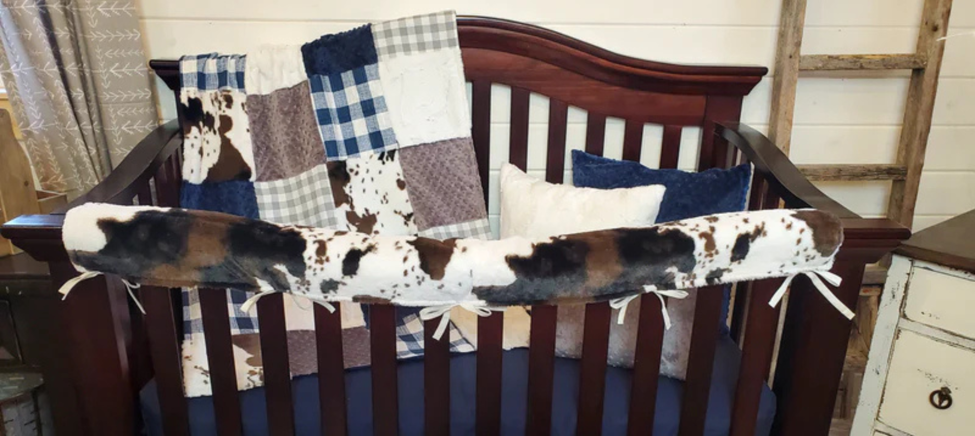 Baby bedding by DBC Baby Bedding Co, Cow print, navy check, tan check. Including a baby patchwork blanket, navy crib sheet, Cow minky Railguard dressed out on a baby crib.