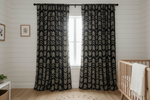 Black curtains with white pattern in a room with a crib and small table.