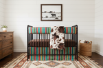 Serape and cow minky western neutral crib bedding on black metal crib in boho western nursery with white shiplap walls